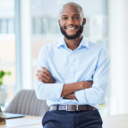 Confident business man standing with arms crossed in an office, looking proud and happy alone at work. Portrait of a smiling, cheerful and professional African male boss working in corporate